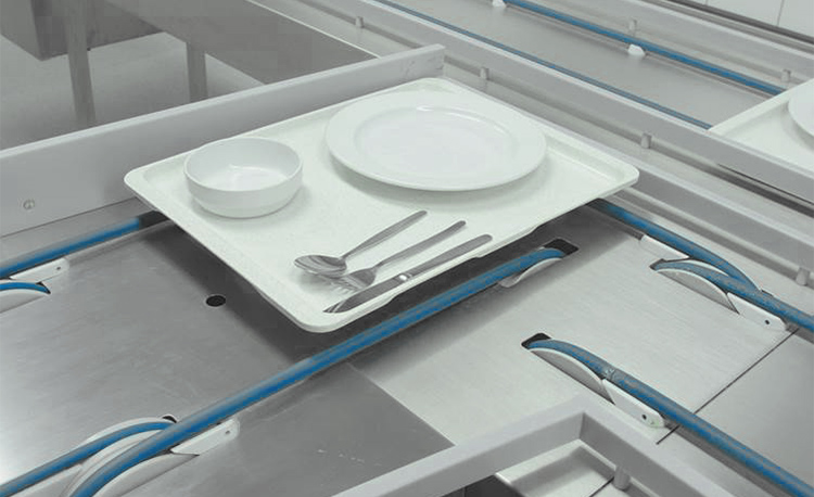 Close-up of a tray on the conveyor of a HOBART FLOW Line autoLINE, automatic washing system for efficient cleaning of dishes and cutlery in a modern dishwashing area, stainless steel construction with blue guides for hygienic workflows.