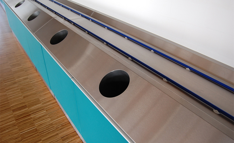 Tray return with drop chutes of a HOBART FLOW Line autoLINE, stainless steel cover with round openings and integrated conveyor for efficient and hygienic workflows in a modern dishwashing area.